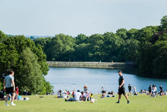 Stock image of a park with lots of people sitting on the grass by a lake