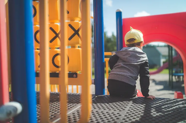 A child with his back to the camera playing on a red and yellow playground