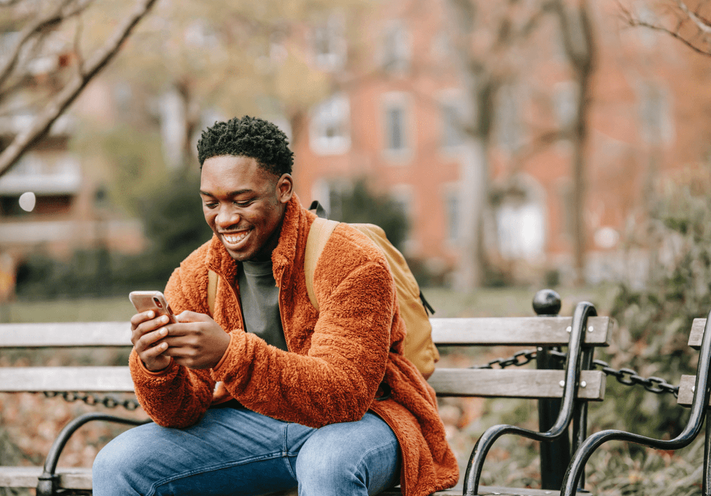 person sitting on a bench smiling while using his phone